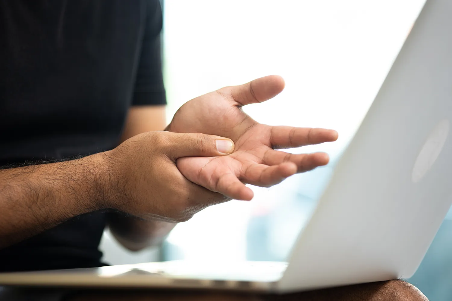 Man working on a laptop with sudden pain in his palm from carpal tunnel