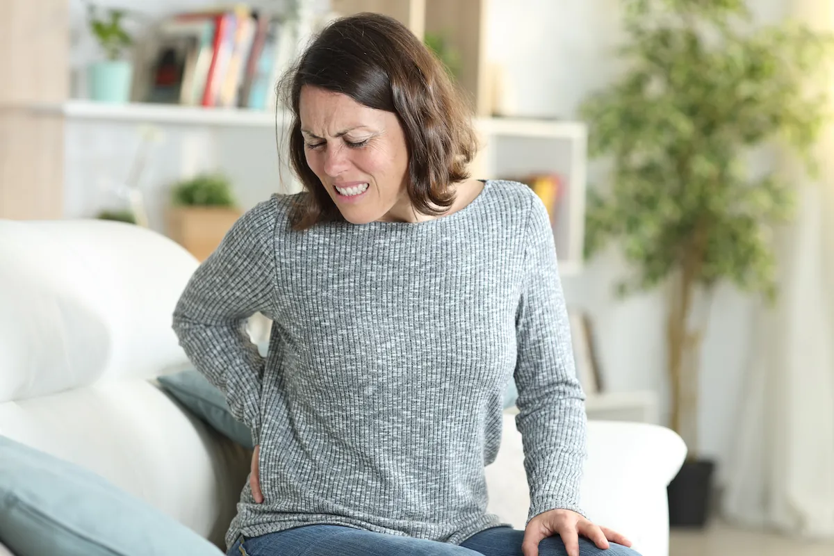 Woman on a couch gripping her lower back in pain
