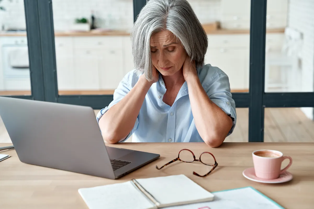 Older woman at a laptop holding her neck