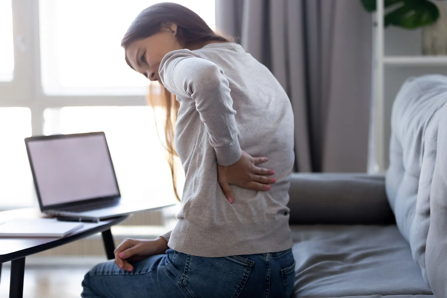 Young woman working from home with sudden pain in her hip